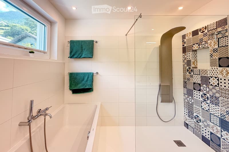 Bathroom. Modern bathroom with a bathtub, glass-enclosed shower, decorative tiles, and two green towels hanging on a rack.