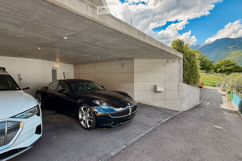 Building. Underground parking area with two parked cars, a white SUV and a black sports car, under a concrete ceiling with visible lighting fixtures.