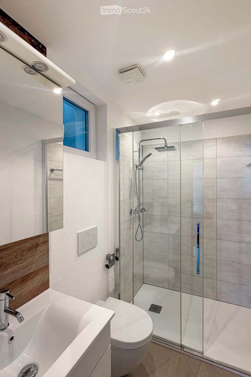 Bathroom. Modern bathroom with a bathtub, toilet, glass-enclosed shower, and a window with blue-tinted glass. Features include a sleek faucet, a towel rack, and recessed lighting.