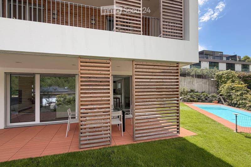 Garden / Outdoor Area. Modern outdoor patio with wooden slatted screens, white chairs, a small table, and a swimming pool in the background.