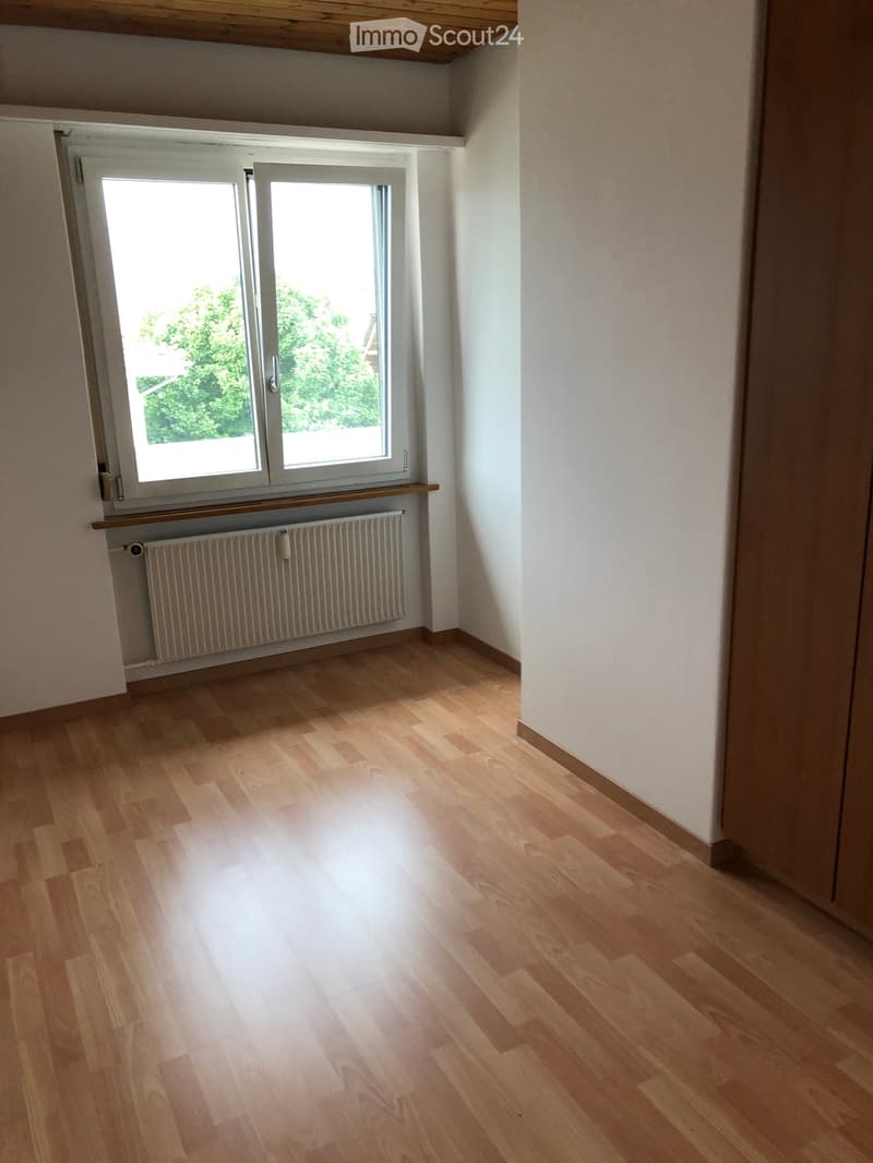 Empty room with wooden flooring, white walls, and a window with a radiator below it.