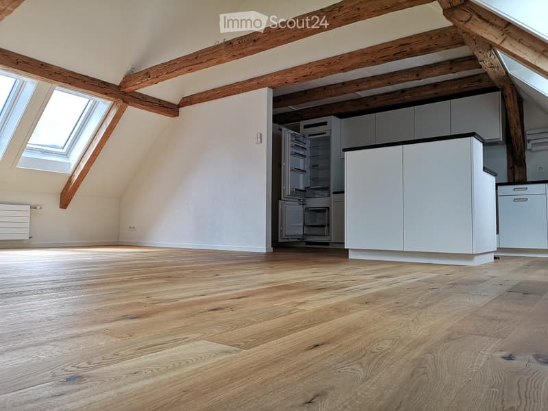 Bright, airy kitchen with exposed wooden beams, white cabinets, and a modern refrigerator. The space features light wooden flooring and large skylight windows.