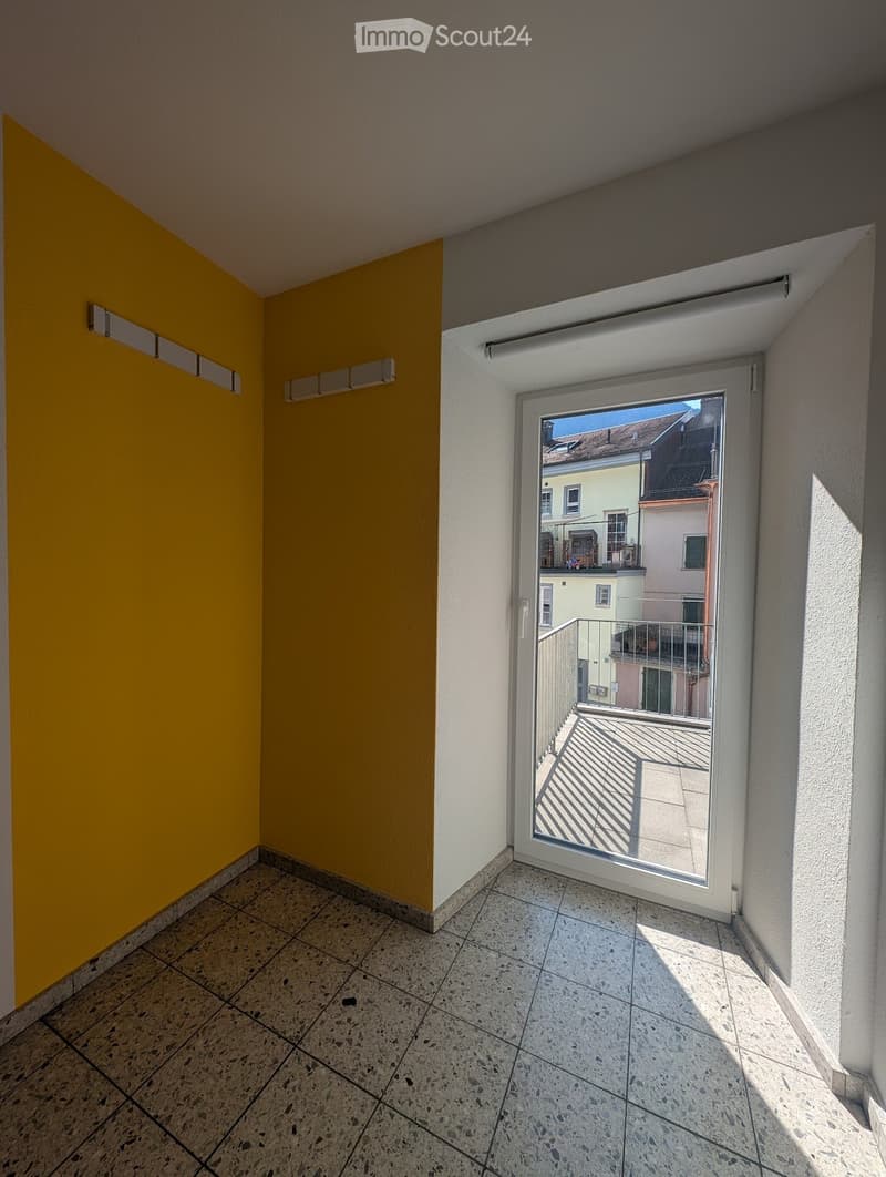 Empty balcony with tiled floor, yellow and white walls, large sliding glass door leading to an outdoor terrace.
