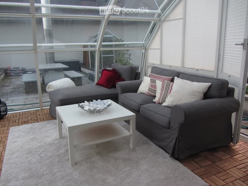 Modern living room with large windows offering a view, featuring a grey sectional sofa, white coffee table, throw pillows, and a decorative bowl on the table.
