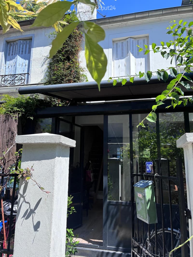A two-story residential building with white walls, multiple windows, and a balcony area. The entrance features a glass door with a black frame, and there is a green mailbox attached to the gate.