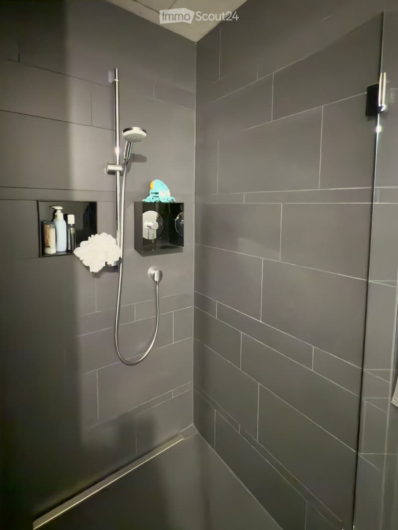grey tiled wall, walk-in shower, bathtub, faucet with shower head, soap and shampoo shelves