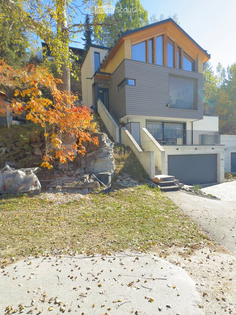 Modern two-story house with yellow and brown exterior, large windows, raised ground floor, two garages.