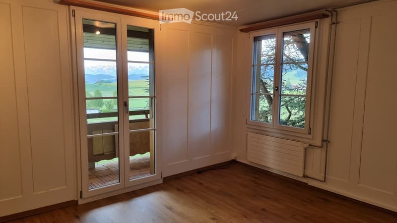 Empty room with wooden flooring, white walls, large windows, and a sliding glass door leading to a balcony with a scenic mountain view.