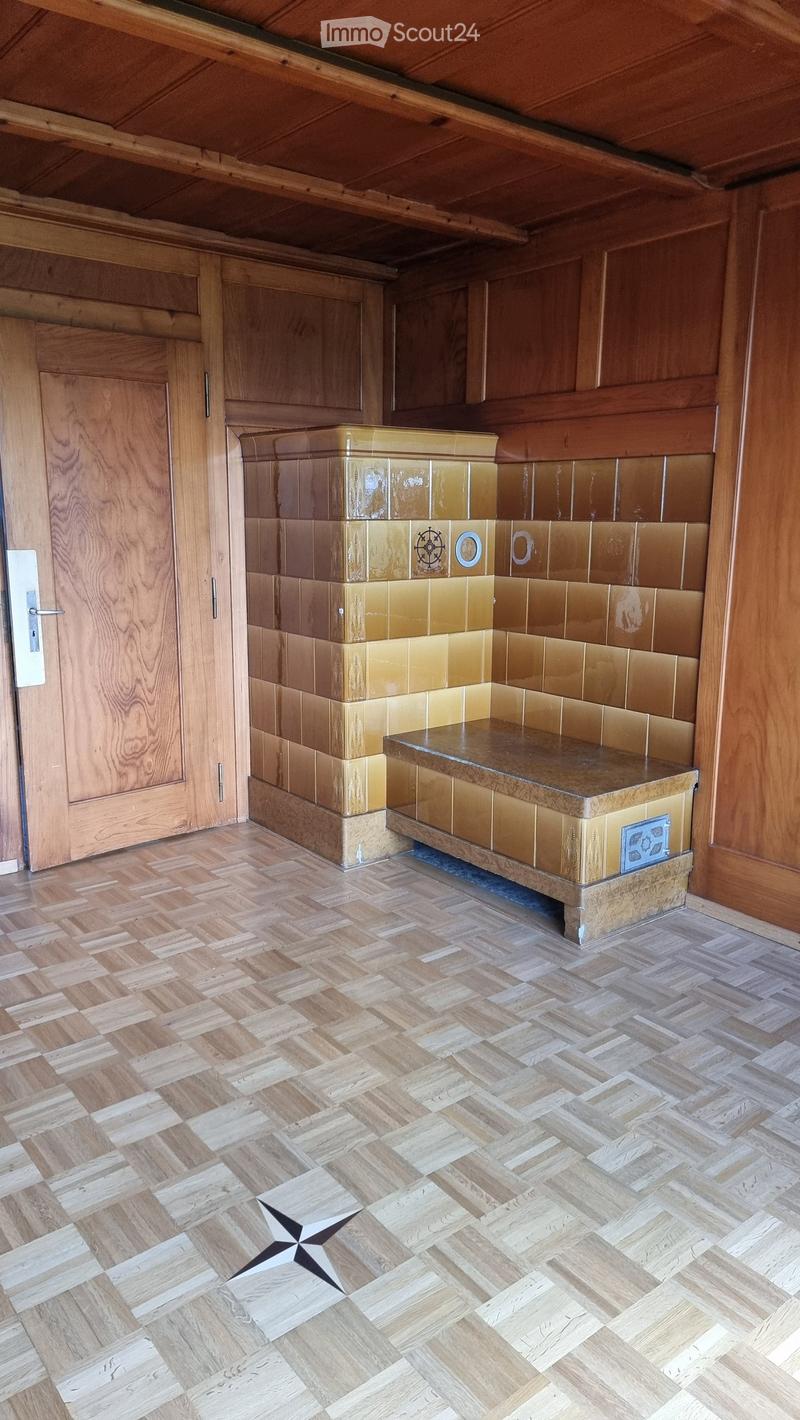 Empty room with wooden walls, herringbone wooden flooring, and a built-in bench with decorative tiles.