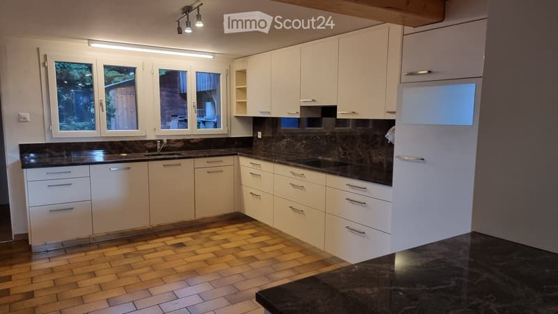 Modern kitchen with white cabinets, dark granite countertops, and a tiled floor. Features a sink, faucet, and a refrigerator.