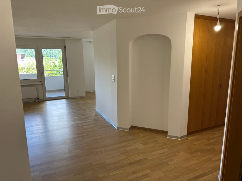 Empty hallway with wooden flooring, white walls, and a door leading to a balcony area.