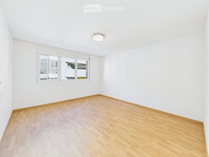 Empty room with white walls, wooden flooring, and large windows with blinds. No furniture or equipment present.