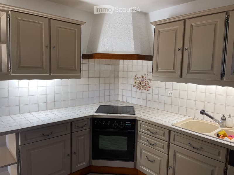 A modern kitchen with white tiled walls, grey cabinets, a sink with a faucet, an oven, and a stove.