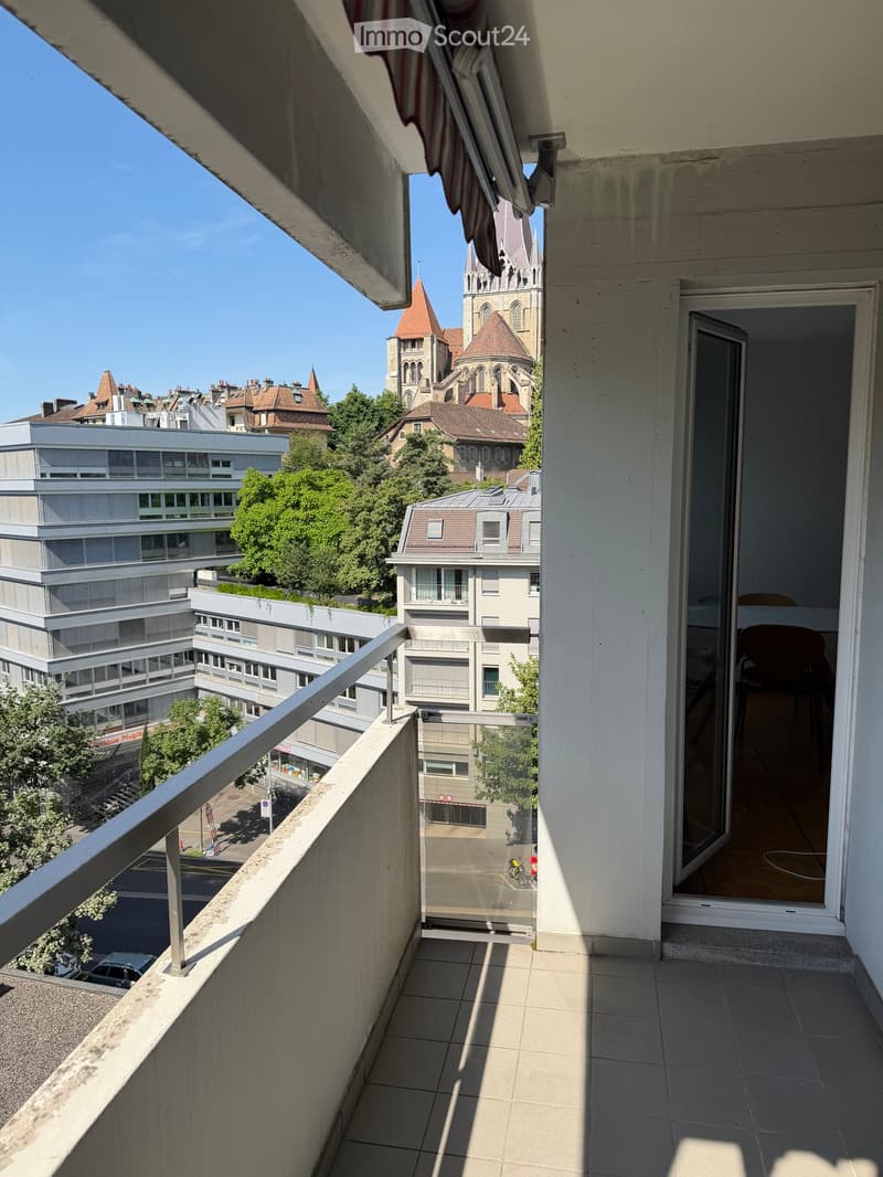 Balcony with tiled floor, metal railing, and a view of a cityscape with buildings, trees, and a prominent church tower.