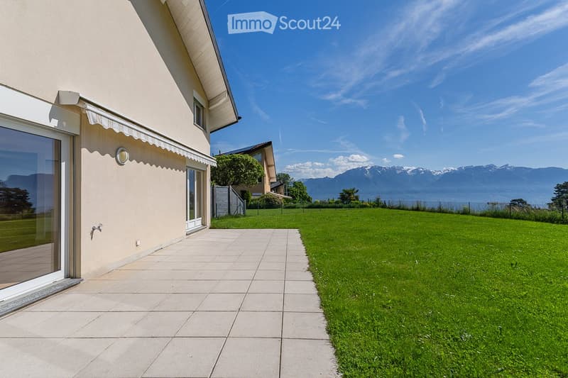 A well-maintained garden with a tiled pathway leading to a house, featuring a scenic mountain view in the background.