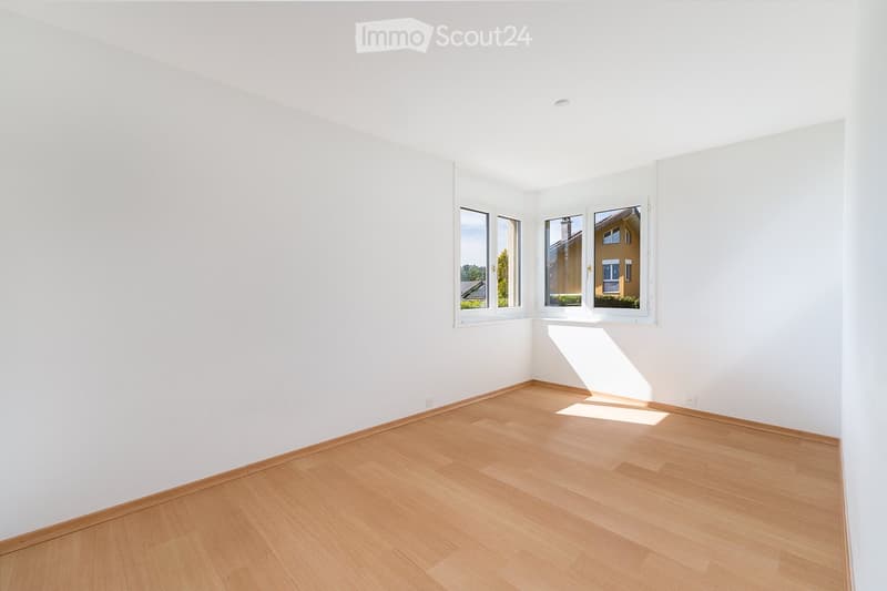 Empty room with white walls and wooden flooring, featuring large windows that let in natural light.