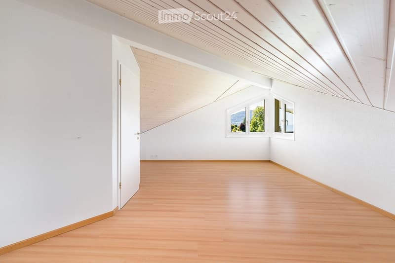 Empty room with white walls, wooden floor, and large windows offering a scenic view.