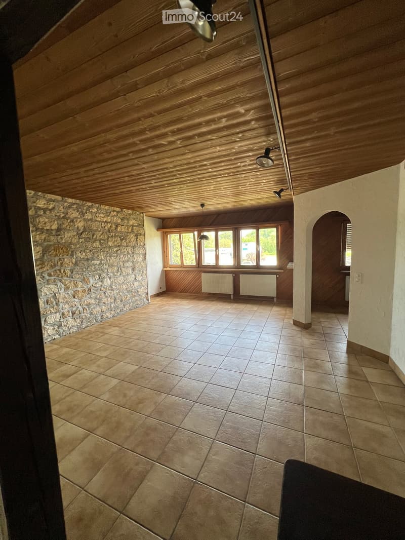 Empty room with wooden ceiling, stone wall, and tiled floor. There are windows and radiators.