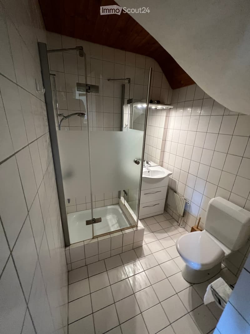 Bathroom with white tiles, glass shower enclosure, white sink, and white toilet.