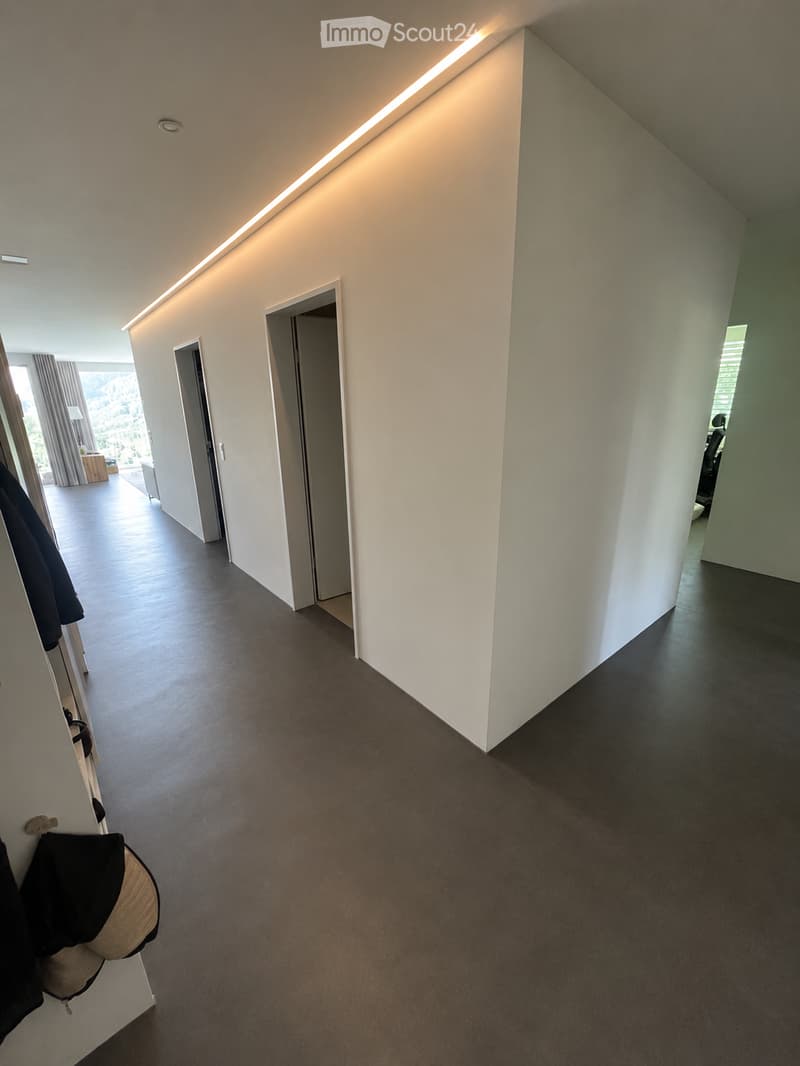 Modern hallway with dark grey carpeted floor, white walls, built-in lighting, and several open doors leading to other rooms.