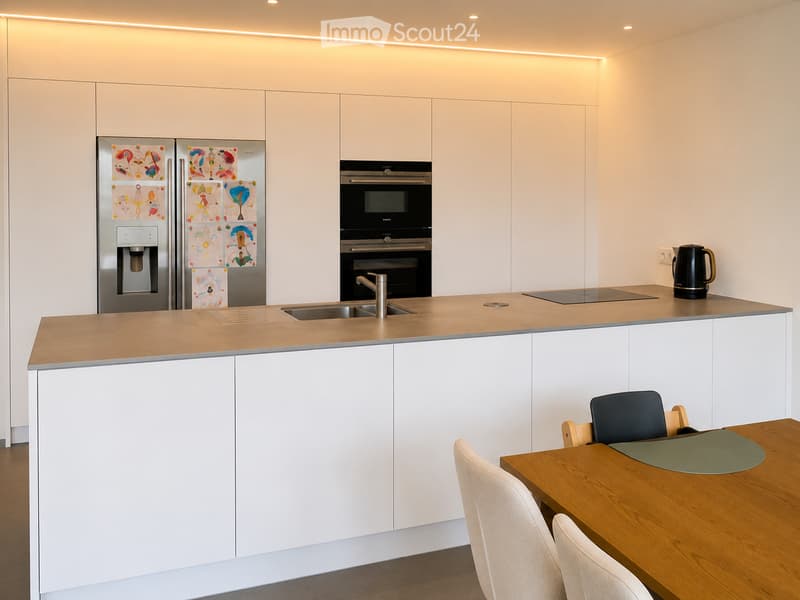 Modern kitchen with white cabinets, stainless steel appliances, a wooden dining table, and chairs.