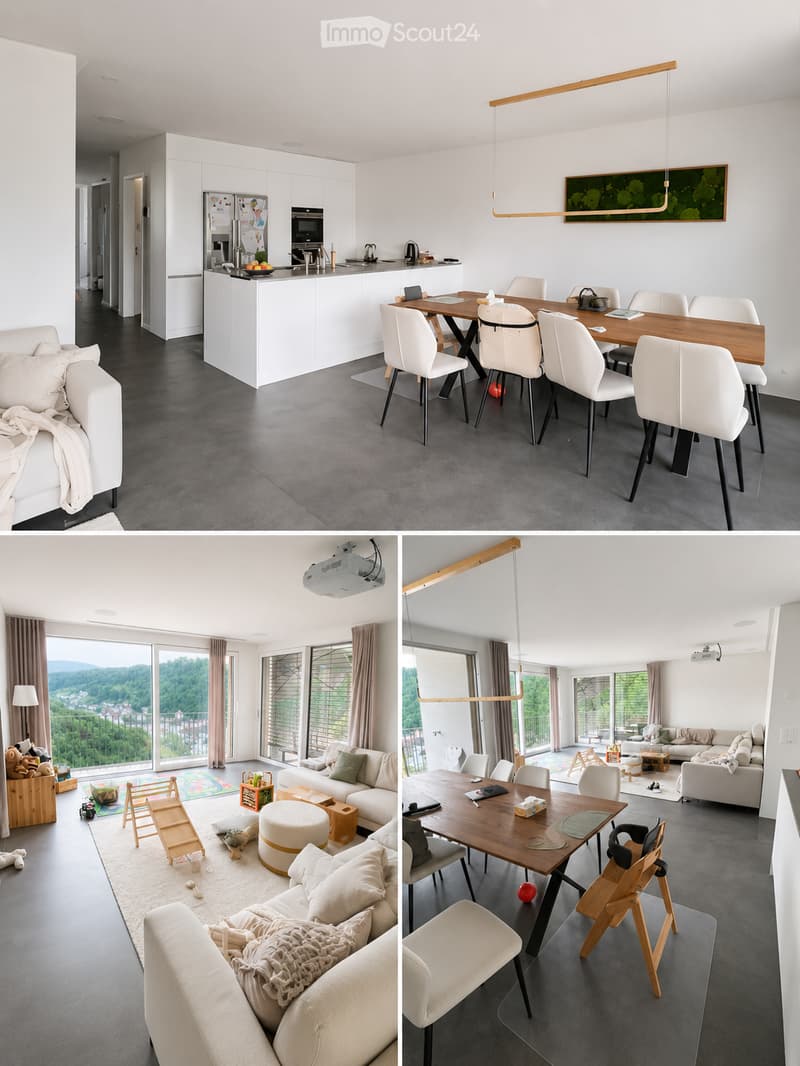 Modern open-plan living and dining area with grey sofa, coffee table, dining table with chairs, kitchen island, and projector. Large windows offer scenic views.