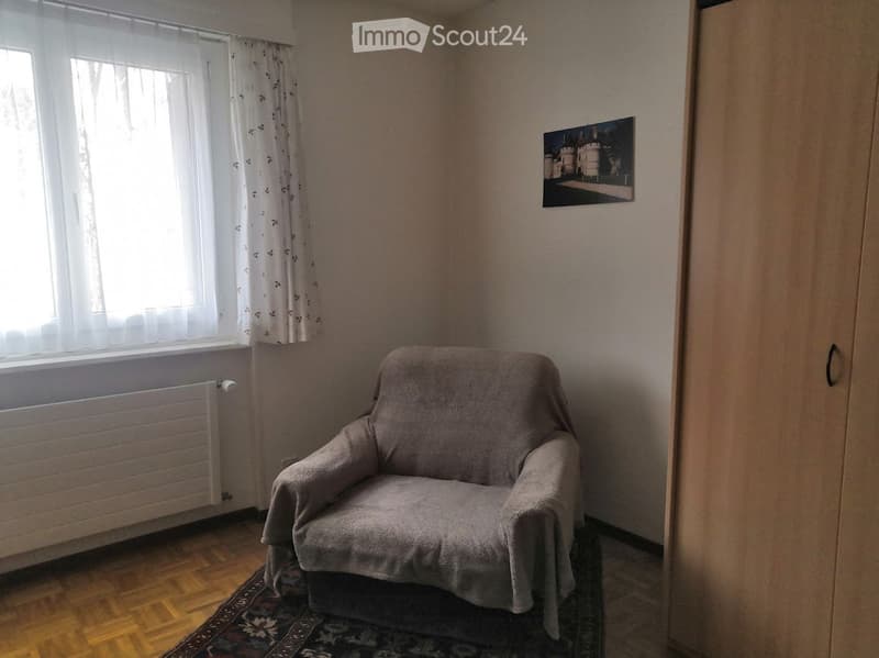 Single chair with throw, white walls, white curtains, picture hanging, hardwood floor, radiator