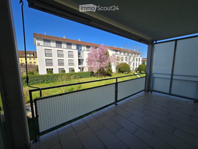 Balcony with tiled floor, metal railing, and a view of a residential area with buildings, trees, and a lawn.