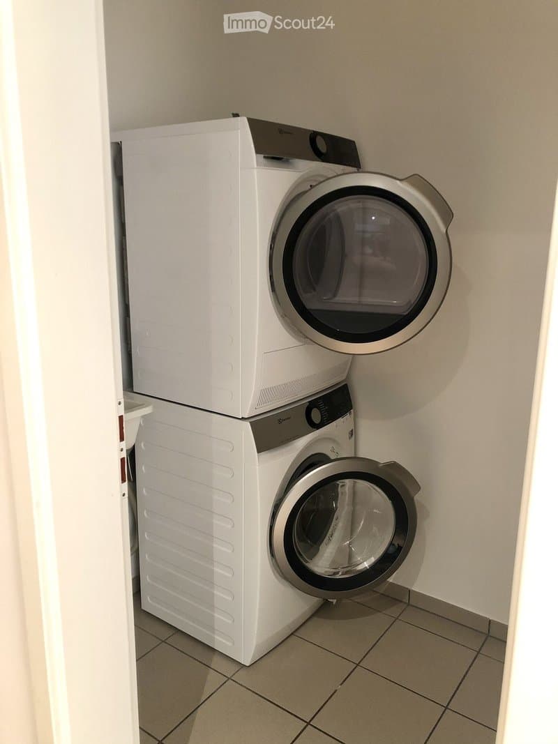 Compact space with stacked white washing machine and dryer, tiled floor, and neutral-colored walls.