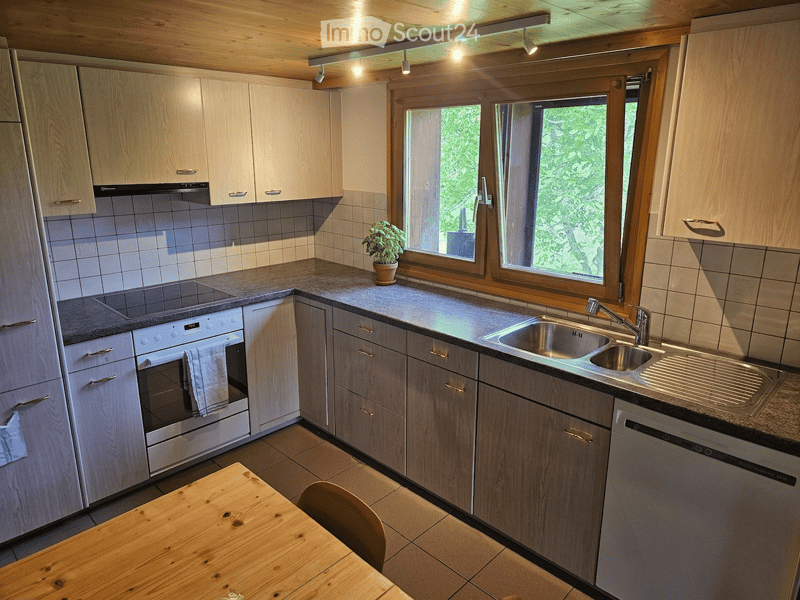 Bright kitchen with wooden cabinets, stainless steel appliances, granite countertops, and a small wooden dining table with a chair.