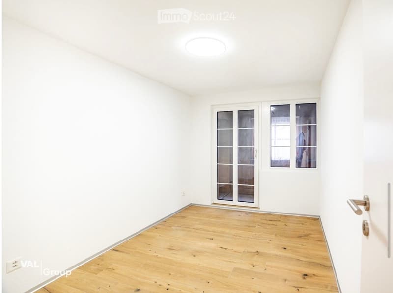 Empty room with white walls, wooden floor, and large windows with glass panels.