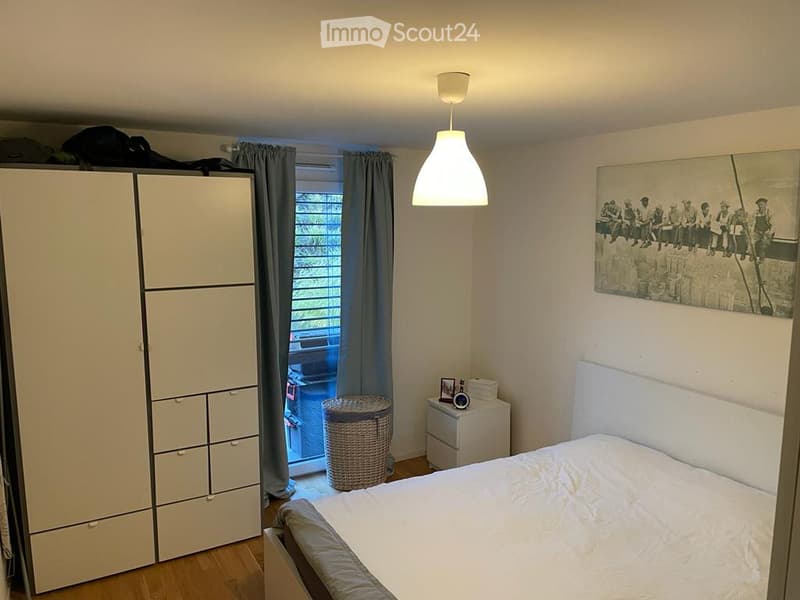 A modern bedroom with a large bed, white wardrobe, nightstand, picture frame on the wall, wicker basket, and curtains covering the window.