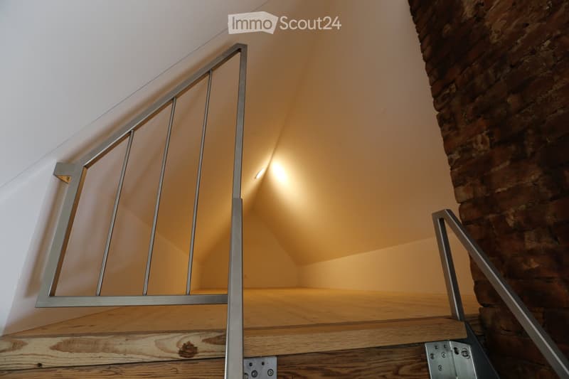 Modern hallway with wooden flooring, exposed brick wall, and sleek metal staircase railing featuring geometric design and integrated lighting.