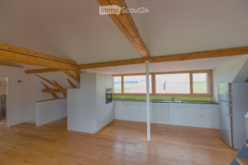 Bright, modern kitchen with white cabinets, wooden flooring, and large windows offering a scenic view. Features include a stainless steel refrigerator, oven, and sink.