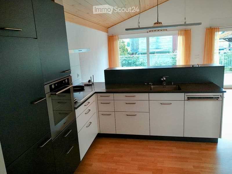 Modern kitchen with dark countertops, white cabinets, stainless steel appliances, and wooden flooring.