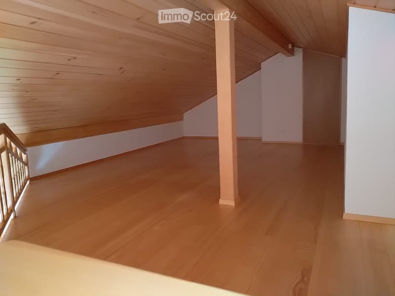 Empty room with wooden flooring and white walls, featuring a staircase with a metal railing on the left side.