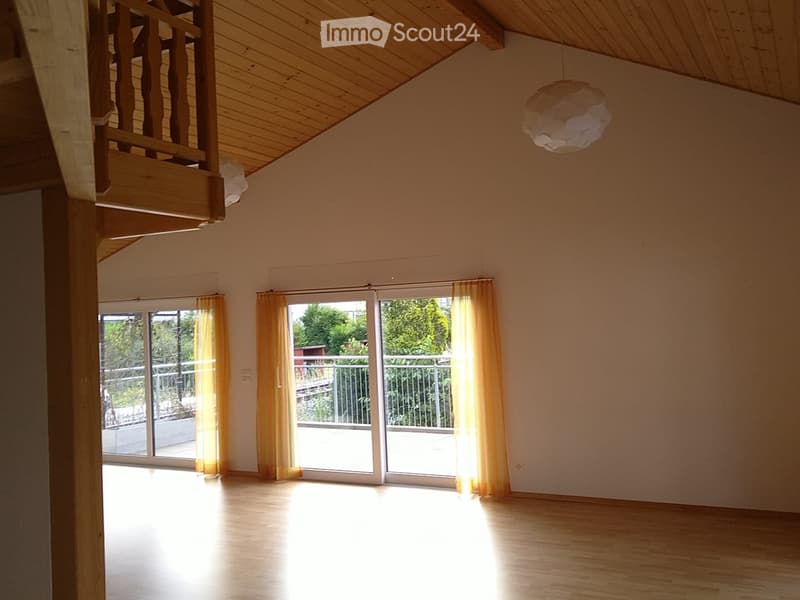 Bright, empty room with wooden flooring, large windows with yellow curtains, and a visible staircase leading to an upper level.