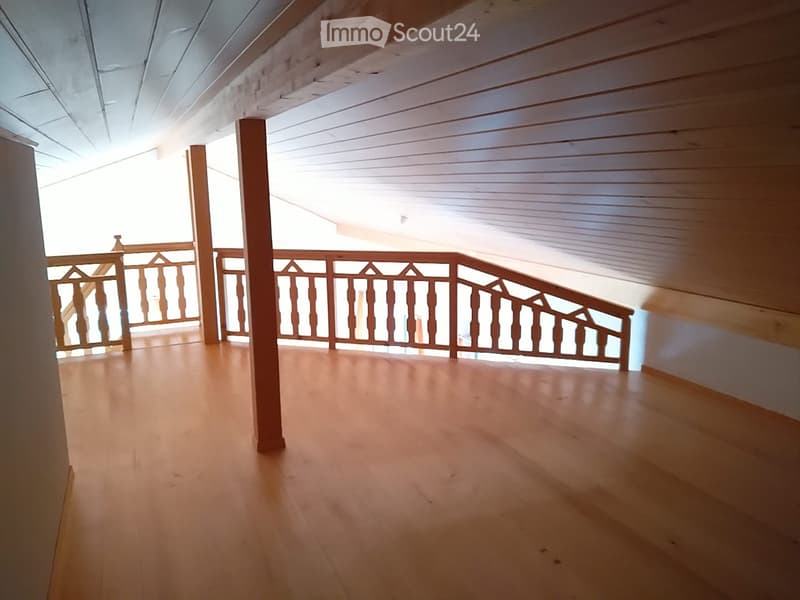 Empty wooden-floored room with a wooden staircase and railing leading to an open area, featuring exposed wooden beams on the ceiling.