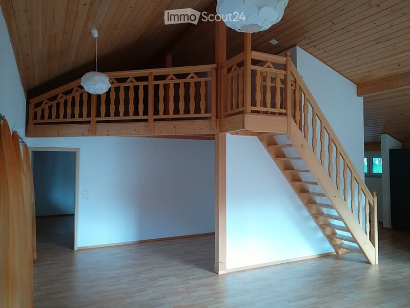 Open, airy space with wooden staircase leading to a loft area, light blue walls, wooden floors, and white pendant lights.