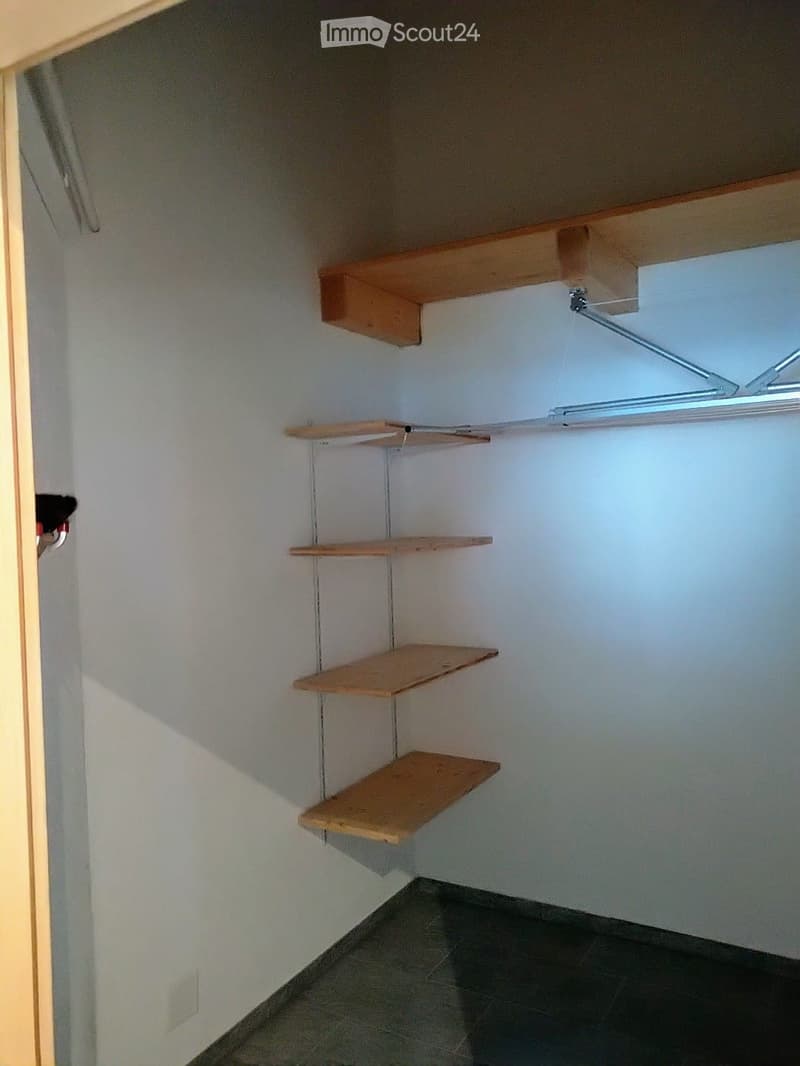 Empty closet with wooden shelves and a clothes rod, white walls, and tiled floor.