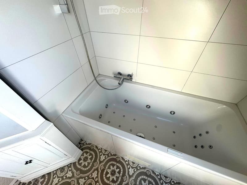 Modern bathroom with a large bathtub, multiple jets, and a sleek faucet. The floor features a decorative tile pattern.