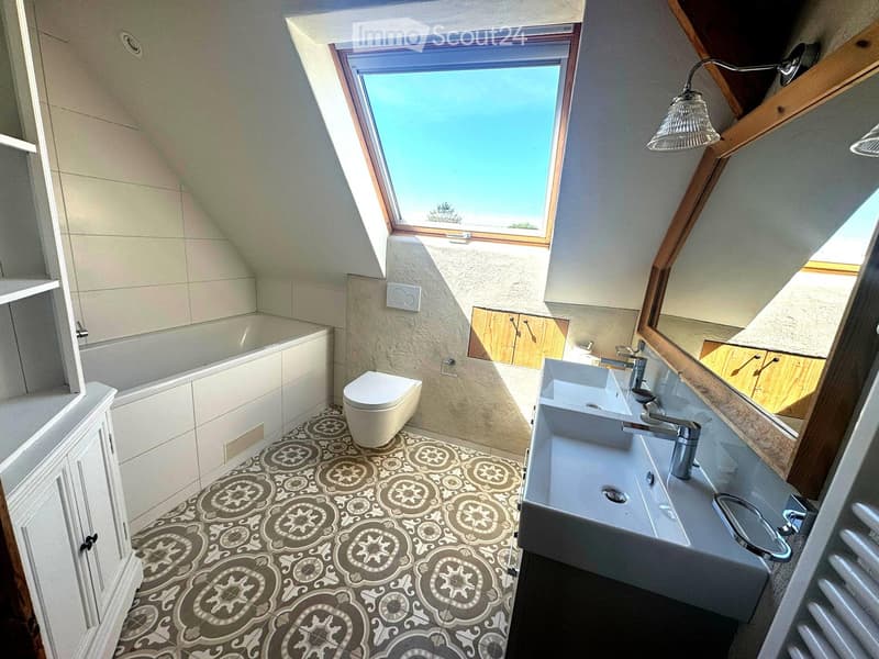 Modern bathroom with a skylight window, bathtub, toilet, sink, mirror, and decorative patterned tile floor.