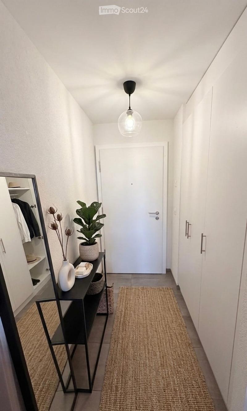 Modern hallway with white walls, a black side table with a vase and plant, a mirror, and a closed door at the end.