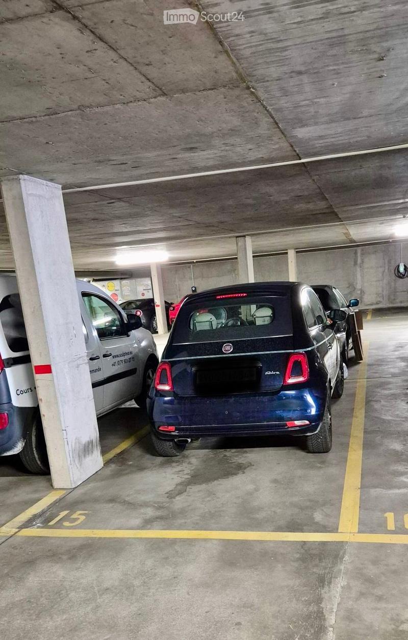 Underground parking area with several parked cars, marked parking spaces, and concrete pillars.