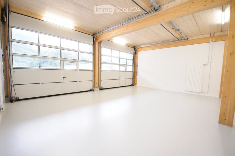 Empty garage with white walls, large garage doors, exposed wooden beams, and a smooth white floor.