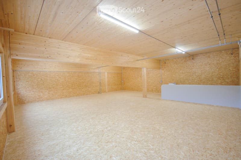 Empty room with wooden walls, ceiling, and floor, featuring exposed wooden beams and a small white cabinet against one wall.