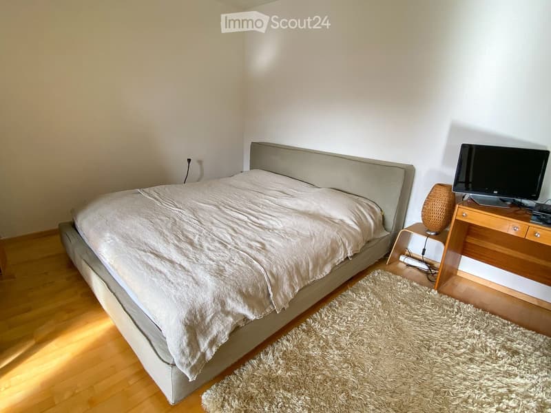 A modern bedroom with a large bed, nightstand, desk, and a shaggy rug on the floor.