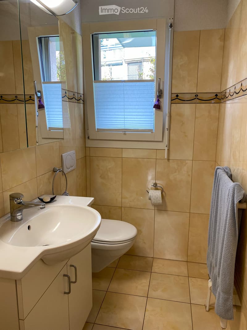 Modern bathroom with beige tiles, a white sink with a chrome faucet, a toilet, a mirror, and a towel hanging on a rack.