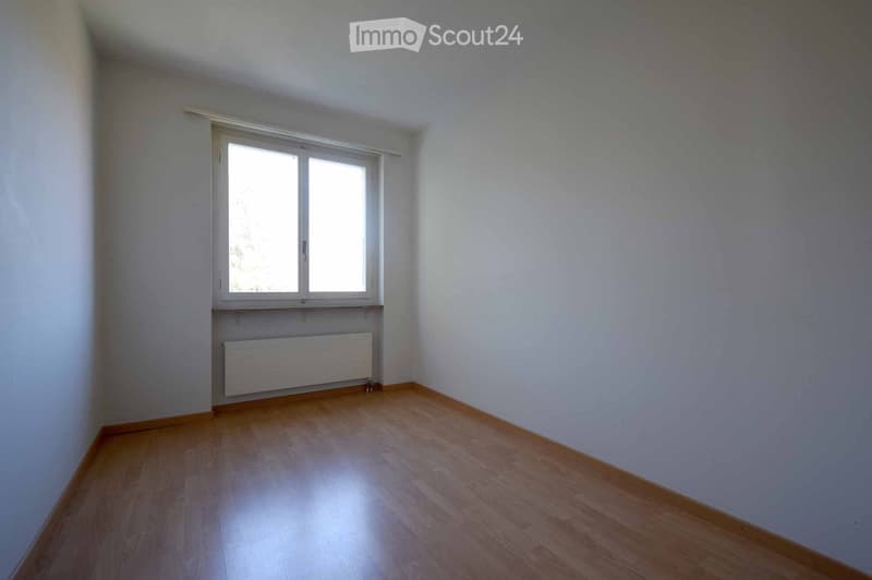 Empty room with wooden flooring, white walls, and a single window with a radiator below it.