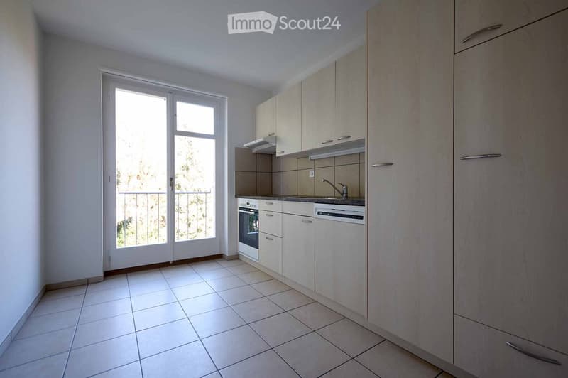 Modern kitchen with white cabinets, tiled floor, and a large window opening to a balcony. Includes an oven, sink, faucet, and dishwasher.
